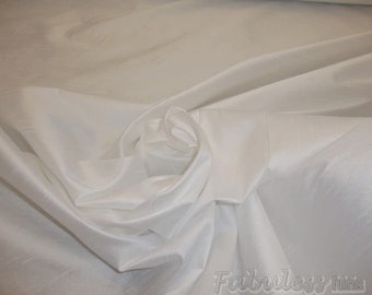 May include: White silk fabric with a smooth, satiny texture. The fabric is draped and folded to create a soft, flowing look.