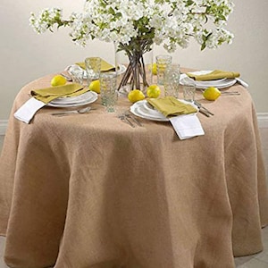 May include: A round, brown burlap tablecloth with a white floral centerpiece and yellow lemons as accents. The tablecloth is set with white plates, yellow napkins, and clear glasses.