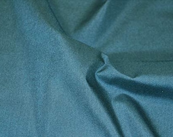 May include: Close-up of teal fabric with a soft, textured appearance. The fabric is folded, creating shadows and highlights that emphasize its texture. The color is a muted teal, with subtle variations in tone across the surface.