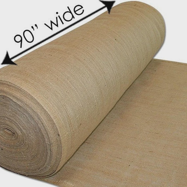 Puede incluir: Se muestra un rollo de tela de yute natural, de 228,6 cm de ancho. La tela es de color marr&oacute;n claro y tiene una textura gruesa y tejida. El rollo est&aacute; parcialmente desenrollado, revelando el ancho y la textura de la tela.
