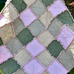 May include: A patchwork quilt with a diamond pattern in shades of pink and green. The quilt is made of various fabrics with different textures and patterns.
