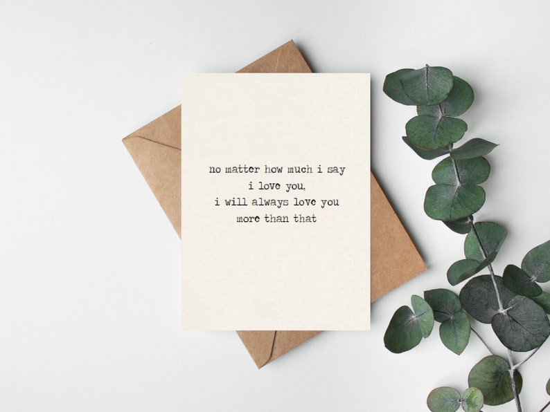 Może przedstawiać: Kremowa kartka z pozdrowieniami z tekstem "no matter how much I say I love you, I will always love you more than that" czcionką maszyny do pisania. Leży na brązowej kopercie, z zielonymi liśćmi w tle.