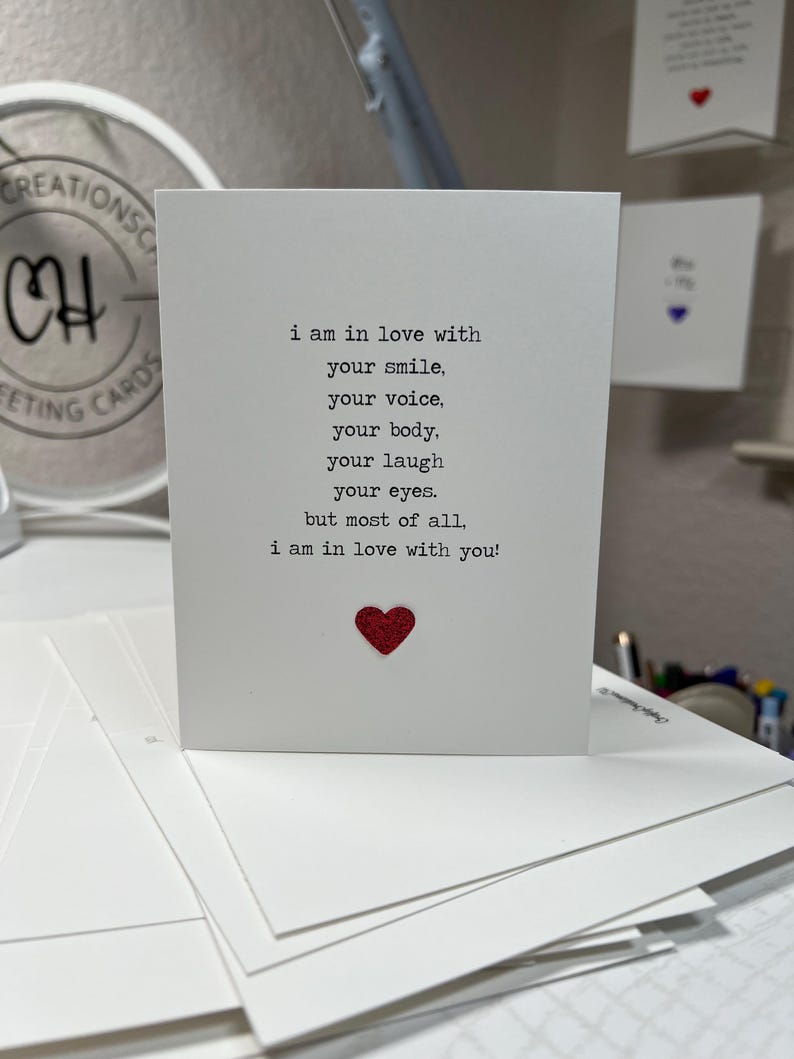 May include: A white greeting card with the text "i am in love with your smile, your voice, your body, your laugh, your eyes, but most of all, i am in love with you!" and a red glitter heart.