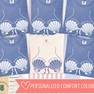 May include: A collection of blue and cream-colored t-shirts. Each shirt features a seashell bra design with the text "Marianna's Beach Bach Miami 2025". The shirts are arranged on a striped background, suggesting a beach theme.