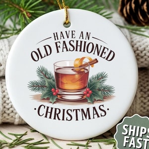 May include: White ceramic Christmas ornament with the text "Have an Old Fashioned Christmas." The ornament features a graphic of an Old Fashioned cocktail with a cinnamon stick and orange peel garnish, surrounded by holly and pine needles.