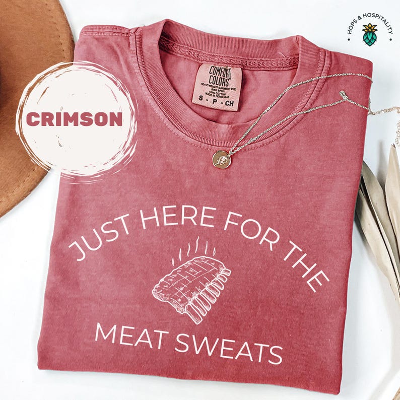 May include: Crimson-colored Comfort Colors t-shirt with the words 'JUST HERE FOR THE MEAT SWEATS' in white. The shirt features a graphic of a rack of ribs. The shirt also has a tag that says 'COMFORT COLORS' and 'S-P-CH'.