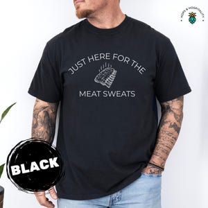 K&ouml;nnte beinhalten: Schwarzes T-Shirt mit dem wei&szlig;en Text "JUST HERE FOR THE MEAT SWEATS" und einer Rippchen-Grafik. Ein "BLACK"-Etikett befindet sich in einem schwarzen Kreis. Ein l&auml;ssiges Kleidungsst&uuml;ck.