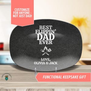 May include: Black oval serving platter with the text "Best Flippen' Dad Ever" and a graphic of crossed grilling tools with flames. The text "Love, Olivia & Jack" is below the graphic.