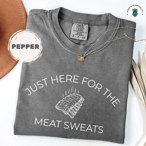 K&ouml;nnte beinhalten: Pfeffergraues T-Shirt mit dem Text "JUST HERE FOR THE MEAT SWEATS" und einer Rippchen-Grafik. Das Shirt ist von Comfort Colors. Eine goldene Halskette liegt &uuml;ber dem Shirt.