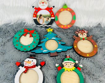 May include: A collection of seven Christmas-themed wooden ornaments. Designs include Santa Claus, a wreath, a Christmas tree, a reindeer, a snowman, and an elf. Each ornament has a circular opening for a photo and a silver string for hanging.