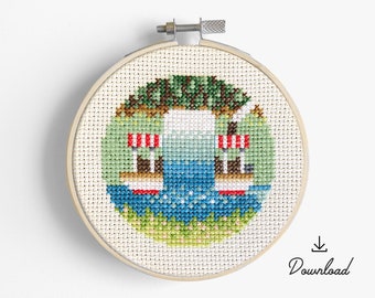 May include: A cross-stitch embroidery hoop with a design of two red and white striped boats on a blue lake with green trees and grass.