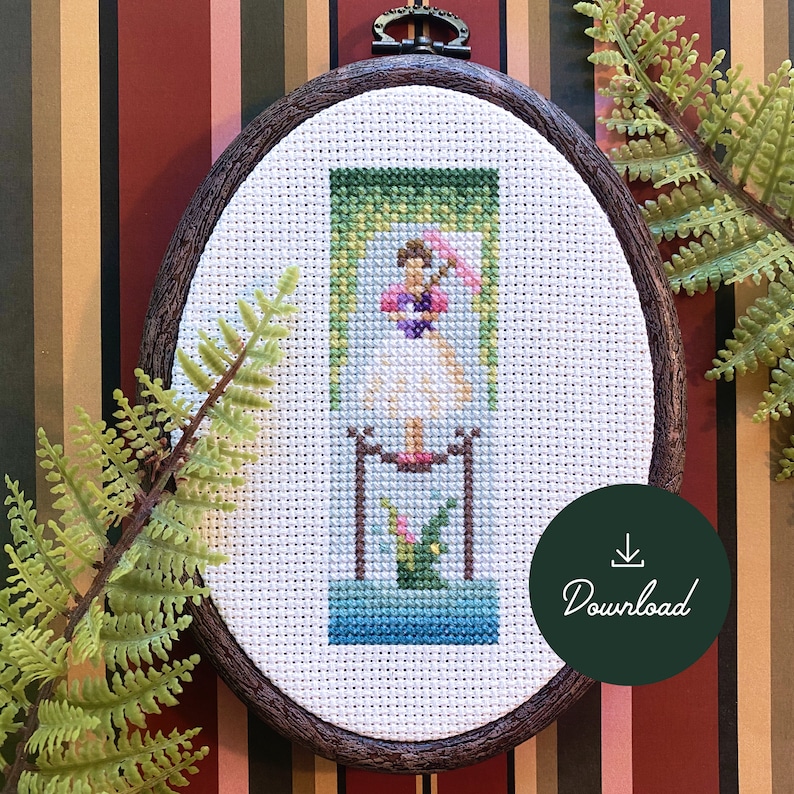 Pu&ograve; includere: Un cerchio da ricamo a punto croce bianco con un design colorato di una persona in piedi su una piattaforma con uno sfondo verde. Il design include una persona con un vestito rosa e un ombrello verde, e una pianta verde con fiori rosa. Il cerchio &egrave; su uno sfondo a strisce con una pianta verde in primo piano.