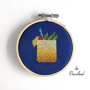 May include: A blue embroidery hoop with a cross-stitch design of a yellow cocktail with a green garnish. The cocktail is surrounded by a blue background.