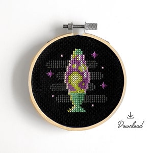 Puede incluir: Un aro de bordado de punto de cruz en blanco y negro con un diseño de lámpara de lava de colores. La lámpara es morada, verde y amarilla sobre un fondo blanco.