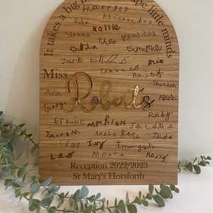 May include: A wooden arch-shaped plaque with the text "It takes a big heart to shape little minds" and the names of children, including "Miss Roberts", engraved in gold. The plaque also includes the text "Reception 2022/2023 St. Mary's Horsforth".