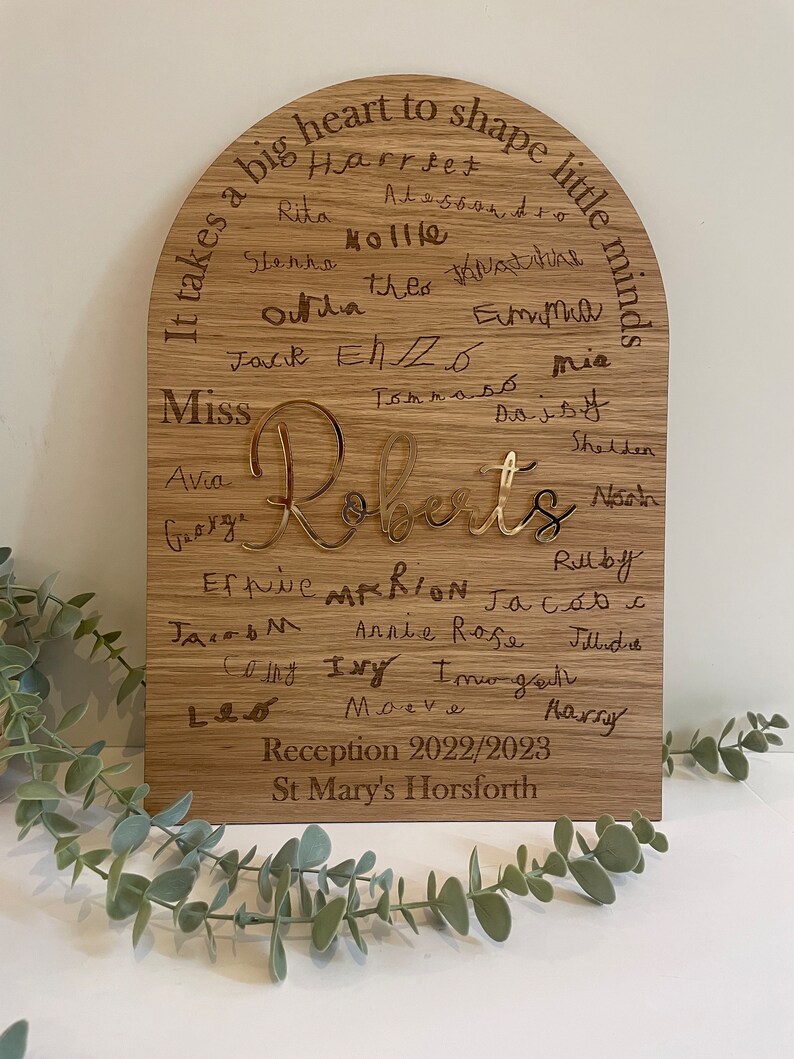 May include: A wooden arch-shaped plaque with the text "It takes a big heart to shape little minds" and the names of children, including "Miss Roberts", engraved in gold. The plaque also includes the text "Reception 2022/2023 St. Mary's Horsforth".