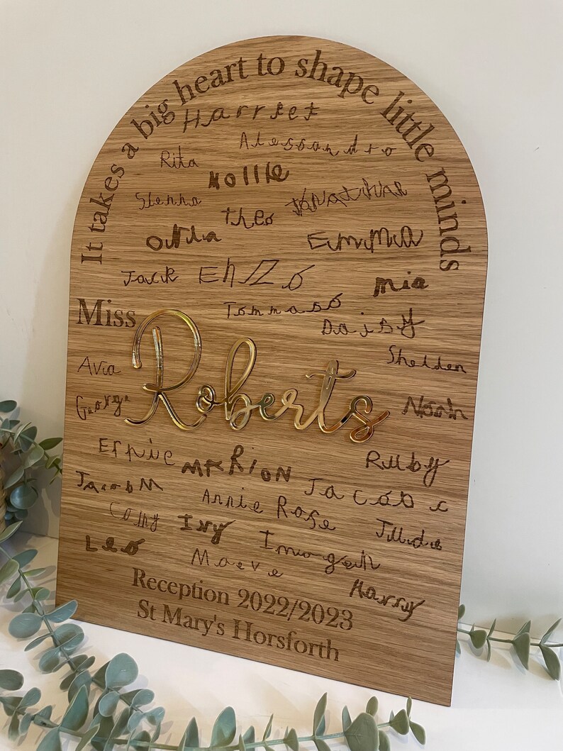 May include: A wooden plaque with a rounded top, featuring the text "It takes a big heart to shape little minds."  The plaque is inscribed with the names of children, including "Roberts", and the text "Reception 2022/2023 St Mary's Horsforth".
