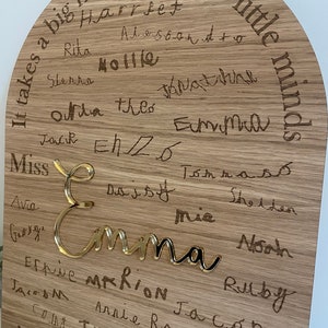 May include: A wooden plaque with the text "It takes a big heart to shape little minds."  The plaque is decorated with a gold-colored name "Emma" and many other names written in cursive.