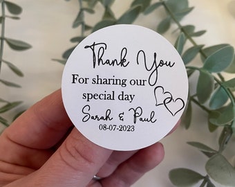 May include: White round thank you sticker with black text that reads "Thank You for sharing our special day Sarah & Paul 08-07-2023" with two black hearts.