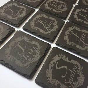 Può includere: Un set di sottobicchieri in ardesia nera con cornici incise decorative e nomi personalizzati. I nomi includono Taylor, Debbie, Kim, Jill, Jan e Sandra.