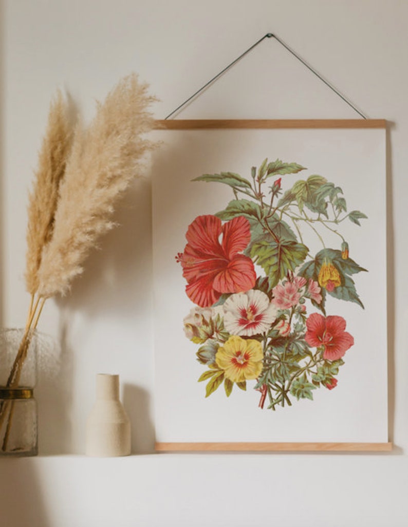 May include: A botanical print featuring a vibrant bouquet of hibiscus and other flowers in shades of red, yellow, and pink, with green foliage. The artwork is displayed on a white background and framed with a wooden hanger.