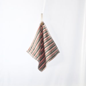 May include: A striped kitchen towel hanging on a hook. The towel is pink, green, and black with white stripes.
