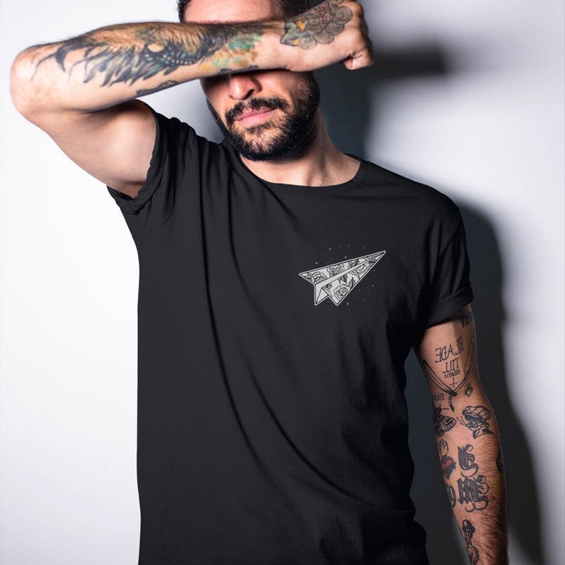 May include: Black t-shirt with a white paper airplane graphic. The airplane is filled with a floral pattern.