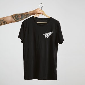 May include: Black t-shirt with a white paper airplane graphic on the front. The airplane is made of folded paper and has a detailed design.