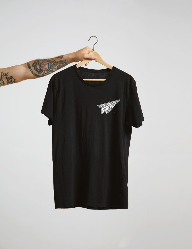 May include: Black t-shirt with a white paper airplane graphic on the front. The airplane is made of folded paper and has a detailed design.