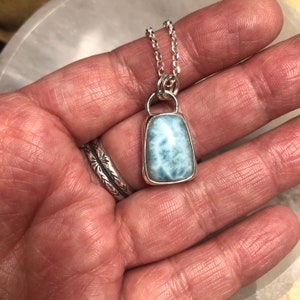 Puede incluir: Un collar de cadena de plata con un colgante que presenta una piedra preciosa azul claro y blanca engastada en un bisel de plata.