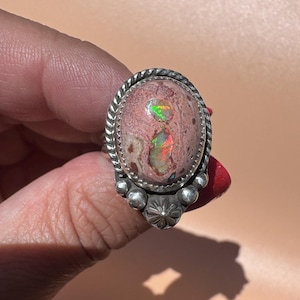 Op de afbeelding: Een zilveren ring met een ovale, roze-bruine steen met twee ingebedde iriserende opaalinsluitingen. De zetting is versierd met een gedraaide touwrand en kleine zilveren bolletjes aan de basis, inclusief een centraal stervormig detail.