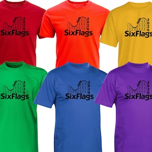 Könnte beinhalten: Eine Auswahl von sechs kurzärmeligen T-Shirts mit Rundhalsausschnitt in Rot, Orange, Gelb, Grün, Blau und Lila. Jedes Shirt zeigt einen schwarzen Grafikdruck einer Achterbahnsilhouette mit dem Text SixFlags und der Jahreszahl 2026 darunter.