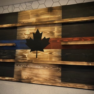 May include: A wooden Canadian flag with a black maple leaf and red and blue stripes. The flag is mounted on a wall and has shelves built into it.