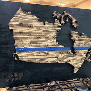 May include: A wooden map of Canada with a blue line across the middle. The map is mounted on a black background and has a gold inscription that reads "SGT. M. ILLNER REG # 3009".