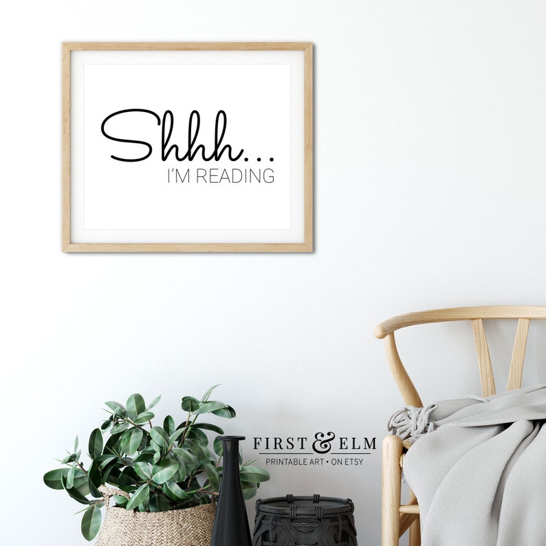 May include: A framed print with the text "Shhh... I'm reading" in black script font on a white background. The frame is light wood.