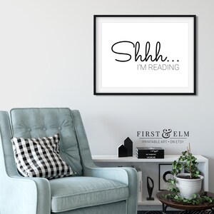 May include: Black and white printable wall art with the text "Shhh... I'm reading". The art is framed in a black frame and is hanging on a white wall.