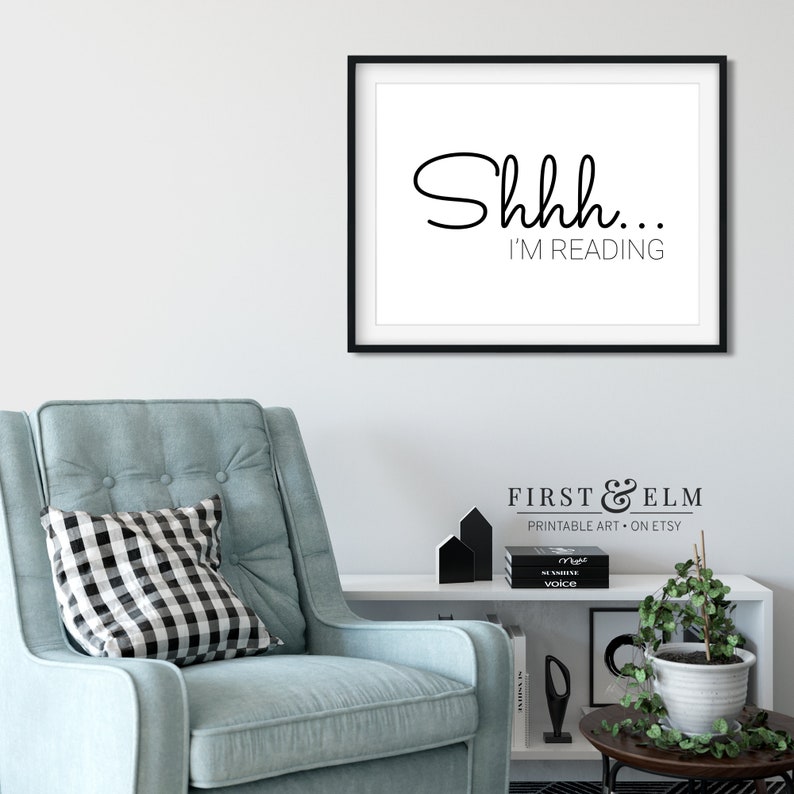 May include: Black and white printable wall art with the text "Shhh... I'm reading". The art is framed in a black frame and is hanging on a white wall.