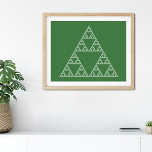 May include: A framed print featuring a white Sierpinski triangle design on a green background. The artwork is displayed in a light brown wooden frame. The print is displayed on a white surface, with a plant and other decor in the background.