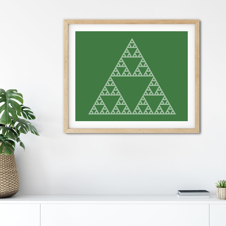 May include: A framed print featuring a white Sierpinski triangle design on a green background. The artwork is displayed in a light brown wooden frame. The print is displayed on a white surface, with a plant and other decor in the background.