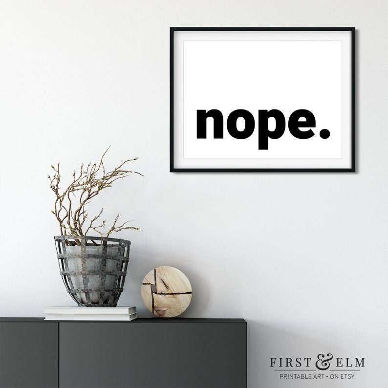 May include: Black and white printable wall art with the word "nope." in bold, black font. The print is framed in a black frame and is hanging on a white wall.