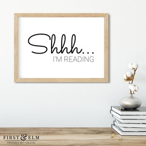 May include: A white framed print with black text that reads "Shhh... I'm reading".