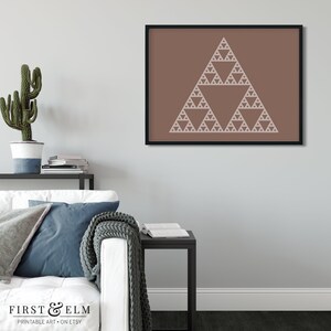 May include: A framed print featuring a white fractal triangle design on a brown background. The artwork is displayed in a black frame, adding a modern touch. The print is part of a home decor collection, suitable for living rooms or offices.
