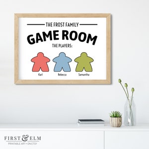 May include: A printable wall art sign with the text "The Frost Family Game Room The Players: Karl, Rebecca, Samantha" with three game piece icons in red, blue, and green.