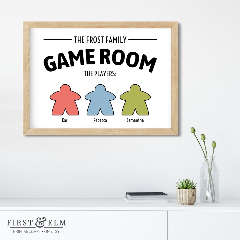 May include: A printable wall art sign with the text "The Frost Family Game Room The Players: Karl, Rebecca, Samantha" with three game piece icons in red, blue, and green.