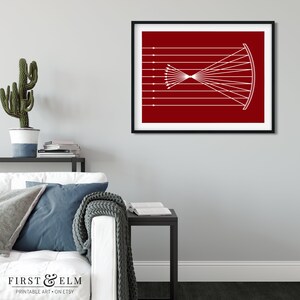 May include: A framed print featuring a white diagram on a red background. The diagram depicts a series of parallel lines converging towards a focal point, then diverging. The print is displayed on a gray wall above a white couch.
