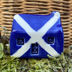 May include: A small blue and white ceramic house with a Scottish flag design. The house has three windows and a chimney.