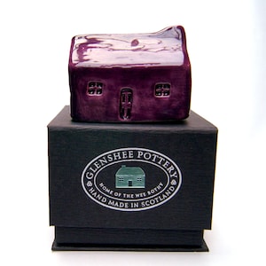May include: A small purple ceramic house in a black box with the text "Glenshee Pottery, Home of the Wee Bothy, Hand Made in Scotland".