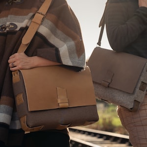 May include: Two people carrying brown leather and felt messenger bags with adjustable straps. The bags have a flap closure with a buckle.