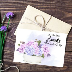 May include: A watercolor illustration of a bouquet of purple and blue hydrangeas in a white pot. The text "It's the little Moments that make life big" is written in black on a light blue background.