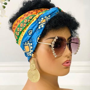 May include: A woman wearing a blue, yellow, orange, and green patterned head wrap, large gold hoop earrings, and clear sunglasses with rhinestones.